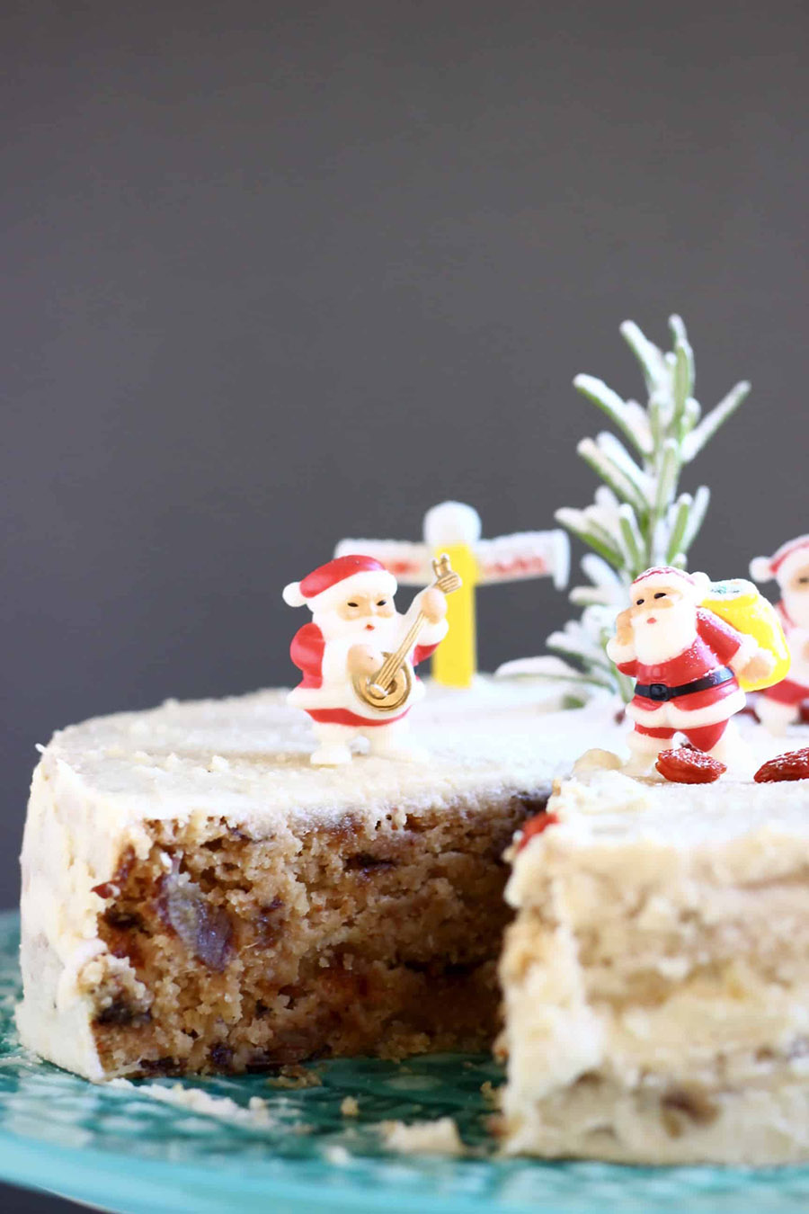 A closeup of an iced fruitcake decorated with miniature santa figurines and dusted with powdered sugar.