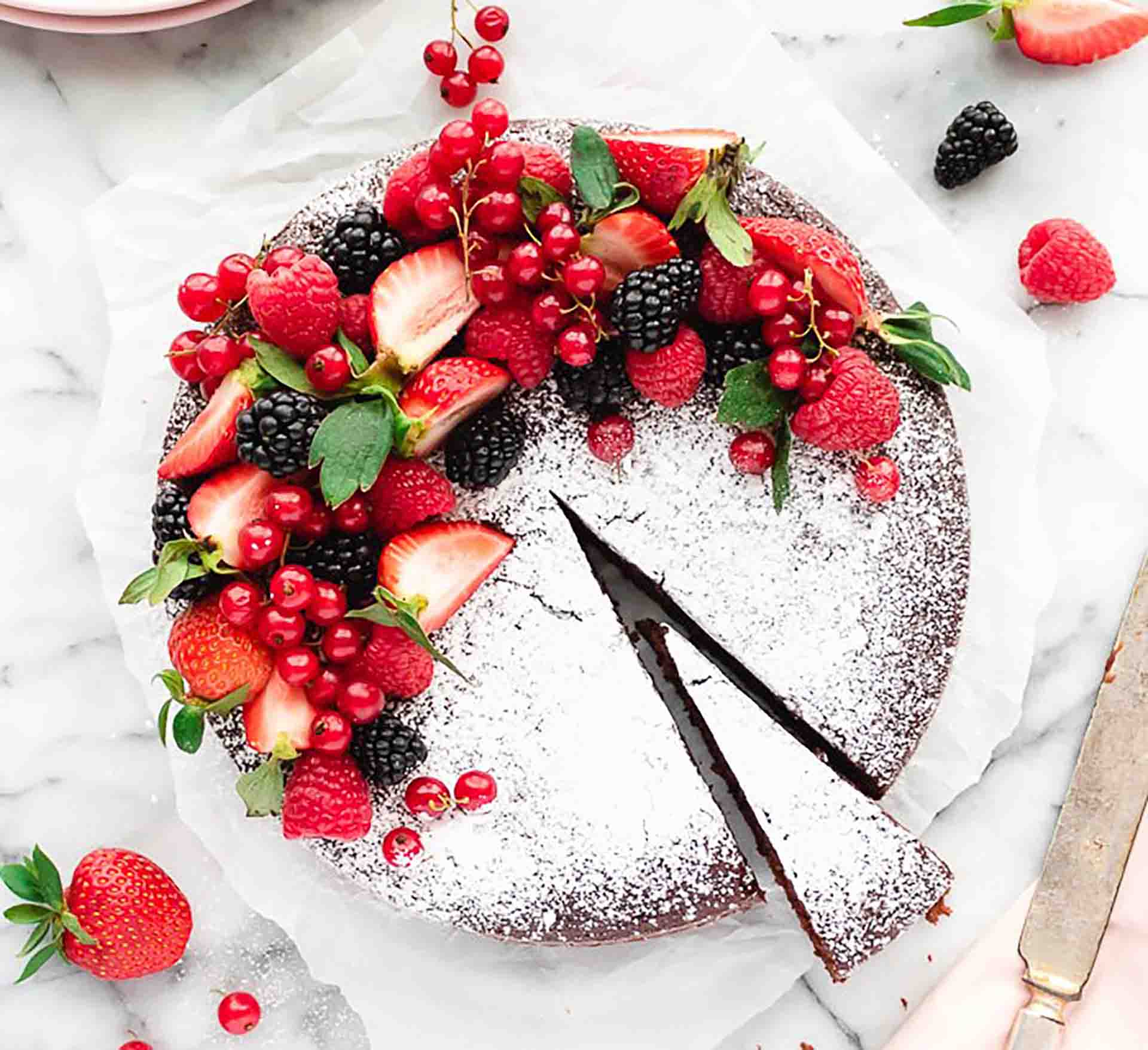 A chocolate cake decorated with various fresh fruits and dusted with powdered sugar.